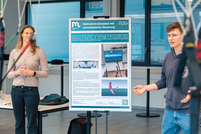 Two people present a poster, “Paraglider Simulator with Sensor‑Based Control”; lines in the foreground.